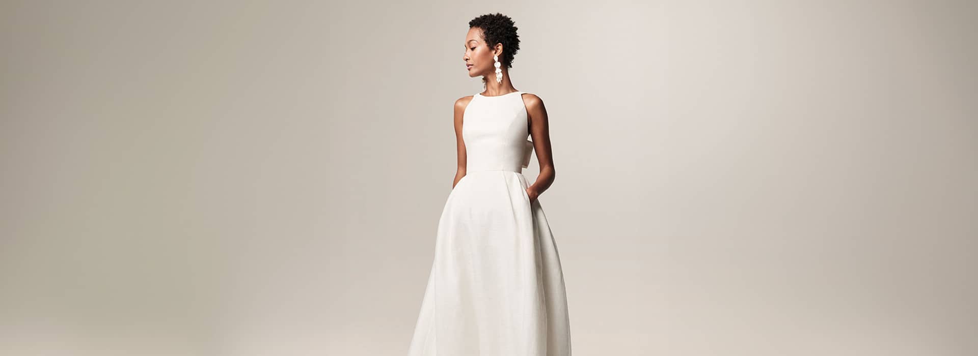 Anabella-Marke-Jesus-Peiro-mobile Stilvolles Model in einem modernen, ärmellosen A-Linien-Brautkleid mit eleganter Haltung auf neutralem Hintergrund.